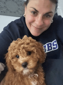 a woman wearing a bb 's sweatshirt holds a small dog