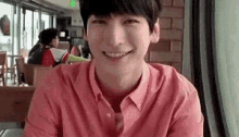 a young man in a pink shirt is smiling while sitting at a table .