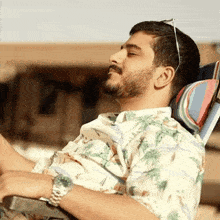 a man with a beard is laying in a chair with his eyes closed and wearing sunglasses .
