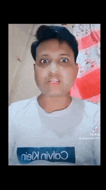 a man wearing a white t-shirt with a blue box on it is making a face .