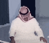 a man in a keffiyeh is sitting at a table with his hands on his knees .