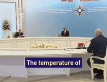 two men sitting at a table with a sign that says " the temperature of "