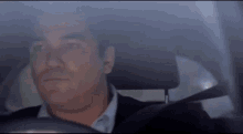 a man in a suit and tie is sitting in the driver 's seat of a car looking out the window .