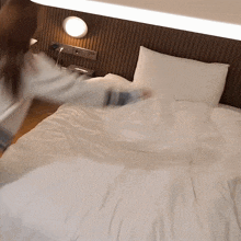 a woman is making a bed with a white comforter