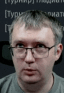 a man wearing glasses and a grey shirt is looking at the camera .