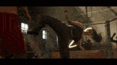 a woman in a black tank top is kicking a man in a boxing ring