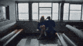 a man and a woman sit on a bench in front of a window