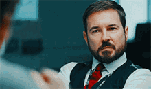 a man with a beard is wearing a vest and tie