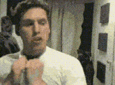 a man in a white shirt is adjusting his tie in front of a mirror