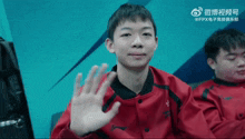 a young man in a red jacket waves his hand in front of a blue background