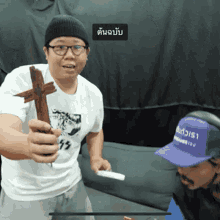 a man in a white shirt holds a wooden cross in front of another man in a purple hat