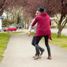 a man in a black hat and a woman in a purple sweater are dancing on a sidewalk