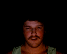 a man with a beard and mustache looks at the camera in the dark