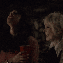 a woman in a pink sweater is holding a red cup in her hand