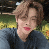 a young man wearing a blue shirt and pink lipstick is taking a picture of himself .