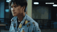 a man wearing a blue shirt with a floral pattern is standing in a dark room .