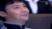 a man in a tuxedo and bow tie is smiling while sitting in a theatre .