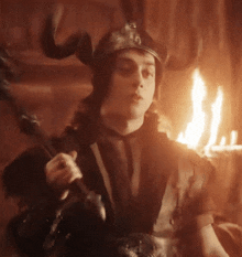 a man wearing a helmet with horns is holding a sword in front of a fire .
