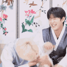 two men are laughing in front of a wall with flowers
