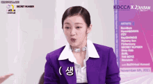 a woman wearing a purple jacket and white shirt is sitting in front of a sign that says secret number