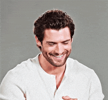 a man with a beard is smiling while wearing a white shirt .