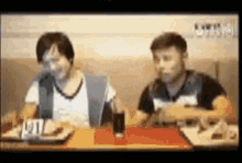 two men are sitting at a table eating food .