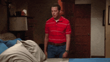 a man in a red and white striped shirt stands next to a bed