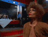 a woman with red lips is standing on a stage with a table in the background