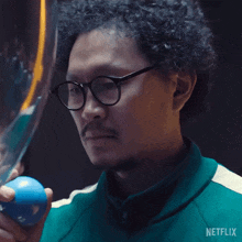 a man with curly hair and glasses is holding a blue ball in his right hand .