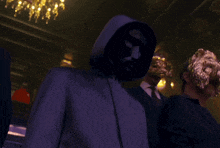 a man in a hooded jacket stands in a dark room with other people