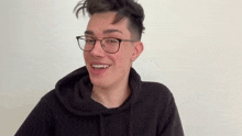 a man wearing glasses and a black hoodie is smiling .