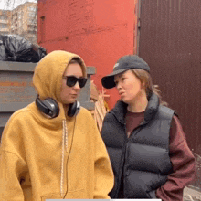 two women standing next to each other one wearing headphones and the other wearing a hat
