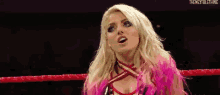 a blonde woman is standing in a wrestling ring wearing a pink outfit .