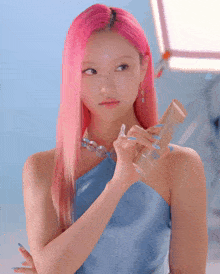 a woman with pink hair and blue nails holds a bottle
