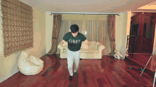 a man wearing a green obey shirt is dancing in a living room