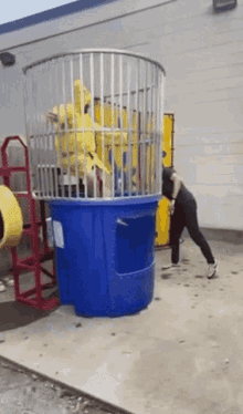 a woman is jumping into a blue bucket with a stuffed animal in it