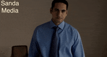 a man in a blue shirt and tie is standing in front of a sanda media logo