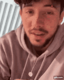 a man with a beard is wearing a hoodie and a necklace while talking .