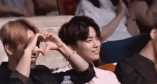 two young men are making a heart shape with their hands while sitting in a theatre .