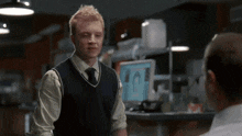 a man in a sweater vest and tie stands in front of a computer monitor