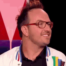 a man wearing glasses and a colorful jacket is smiling and looking at the camera .