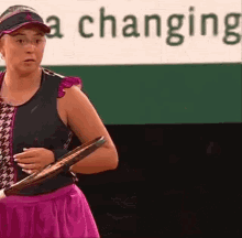 a woman is holding a tennis racket in front of a sign that says a changing