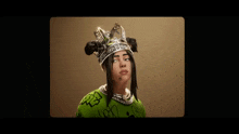 billie eilish is wearing a crown on her head and a green sweater .