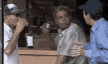 a man in a baseball cap is drinking from a cup while two other men talk to him