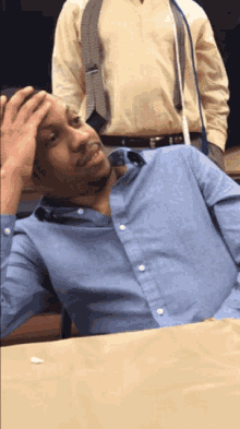 a man in a blue shirt is sitting at a table with his hand on his forehead
