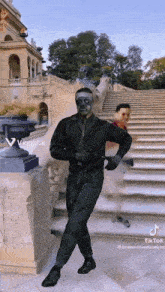 a man with a mask on his face is dancing in front of a staircase .