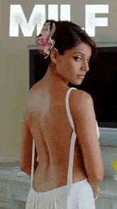 a woman in a white dress with a flower in her hair is standing in front of a television with the word milf written on the top
