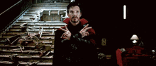 a man in a red cape is standing in front of a staircase and making a peace sign .