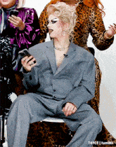a woman in a suit is sitting on a chair and holding a cell phone
