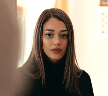 a woman with long hair is wearing a black turtleneck and looking at the camera .